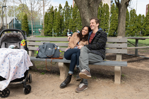 A couple sits on a park bench with their baby stroller beside them